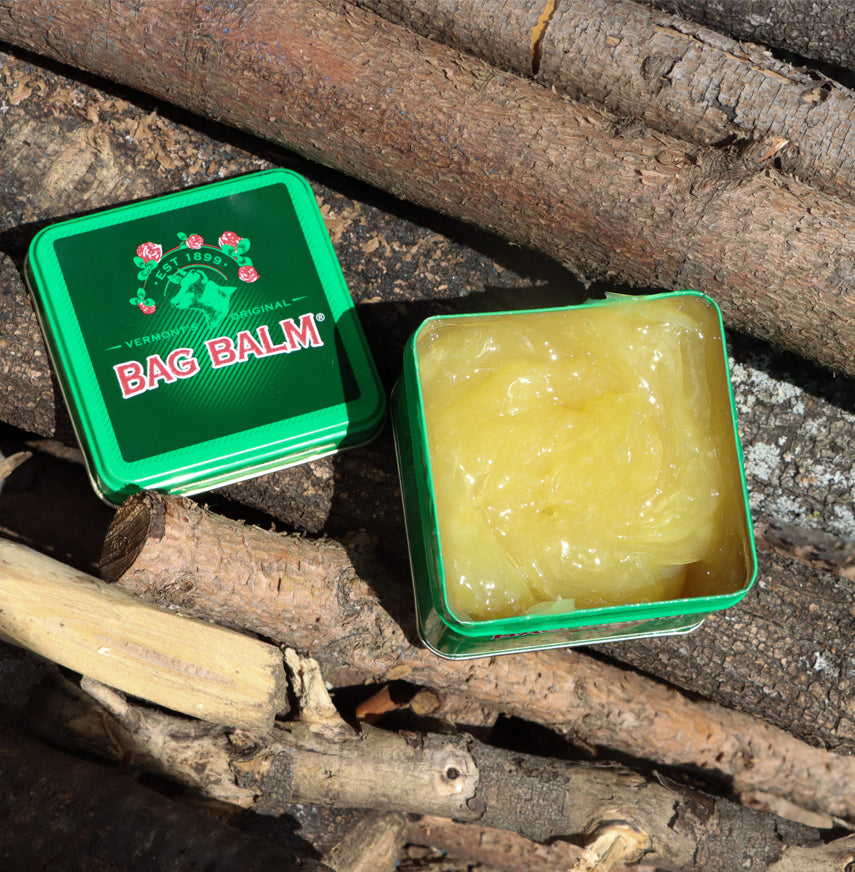 Bag Balm Antiseptic Ointment 8 oz tin. The tin features the classic green design with the Bag Balm logo on the front. The ointment is known for its moisturizing and healing properties. The tin is open on a pile of sticks so you can see the yellow colored balm.